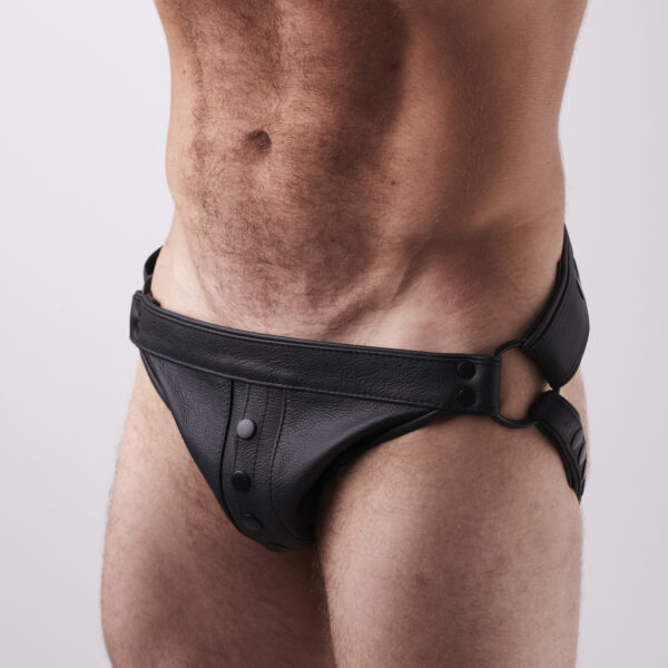 Jockstrap ma szeroki pas w talii, który zapinany jest na rzepy po bokach, oraz elastyczne paski biegnące pod pośladkami. Przód wykonany jest z czarnej ekoskóry na środku z widocznymi czarnymi guzikami na środku.